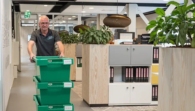 Verhuizer van Top Movers rijdt een rolcontainer met verhuiskratten door een kantoor