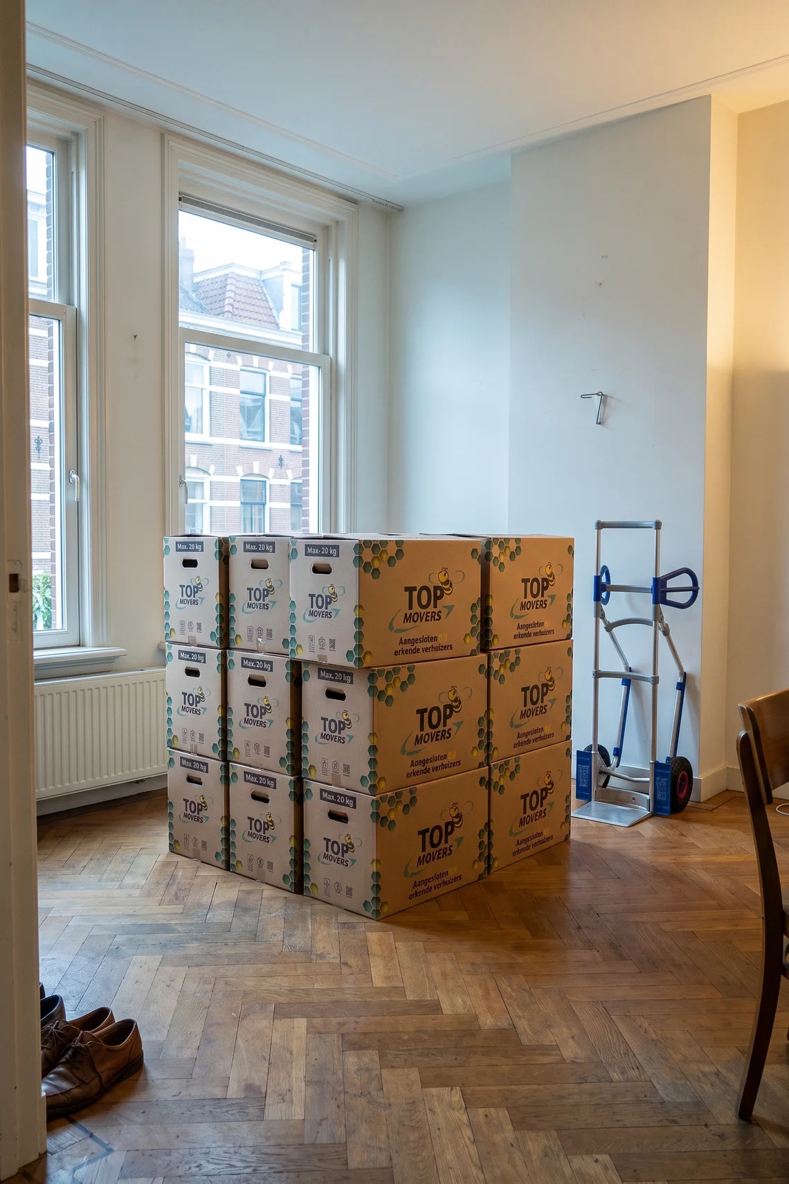 Stapels grote en kleine verhuisdozen van Top Movers in een lege woonkamer