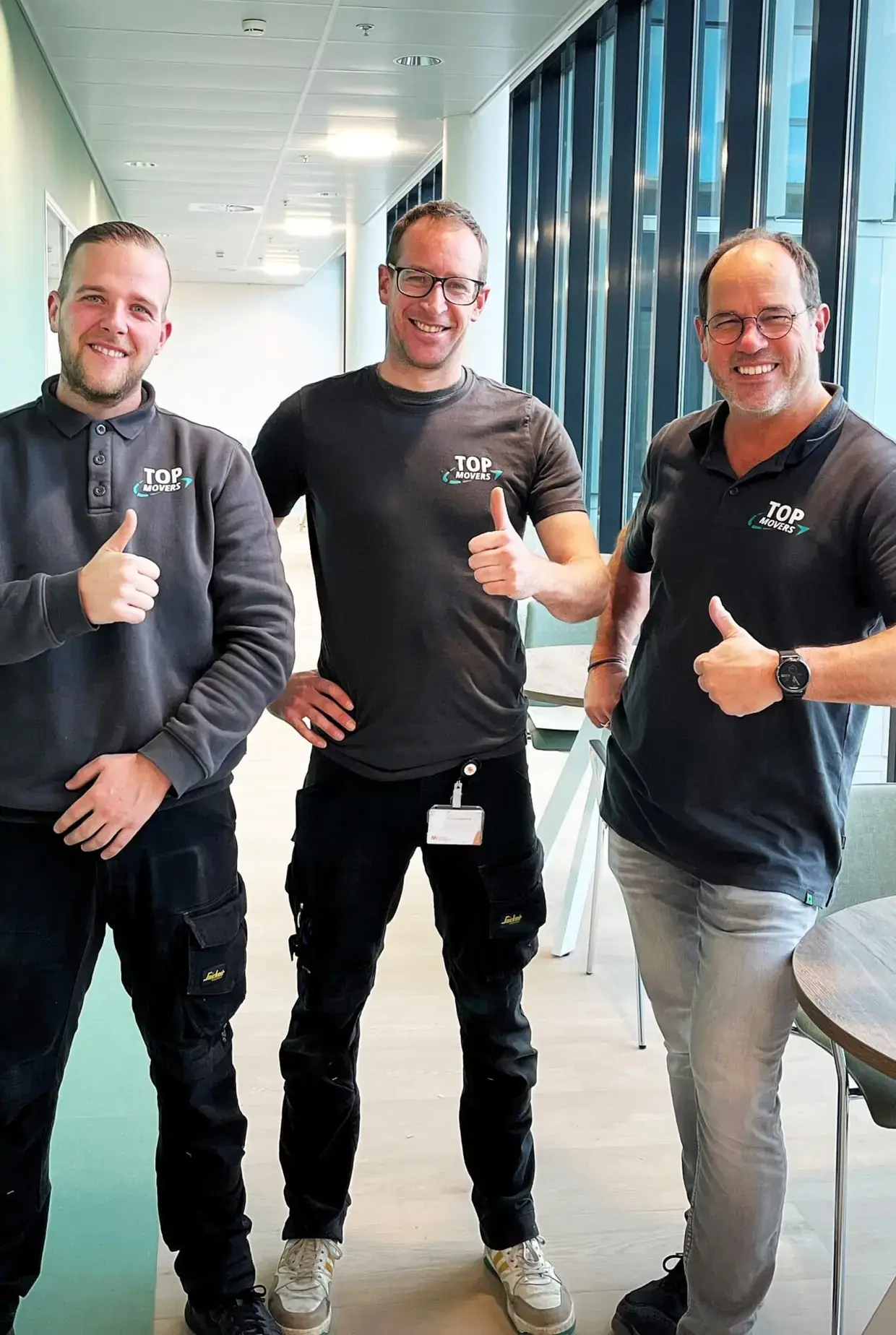 Drie medewerkers van Top Movers met de duim omhoog in een kantoorgang