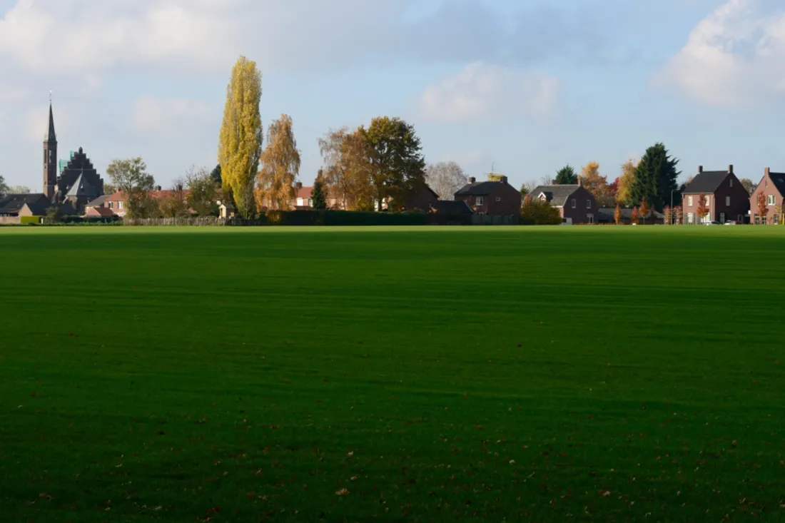 Huizen en een spitse kerktoren aan de rand van Merselo, achter een groen veld