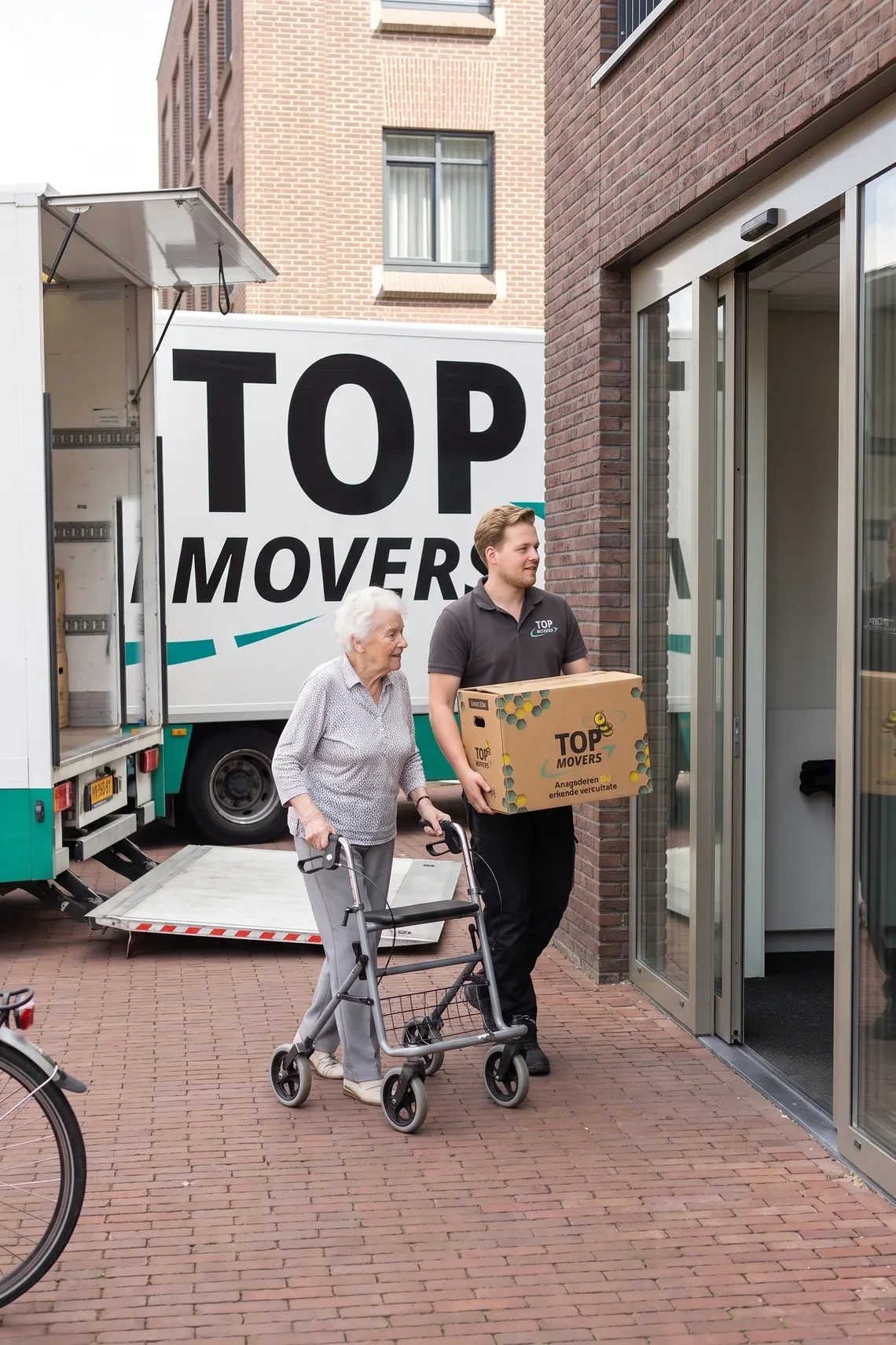 Verhuizer loopt met een doos naast een mevrouw met rollator de seniorenwoning binnen