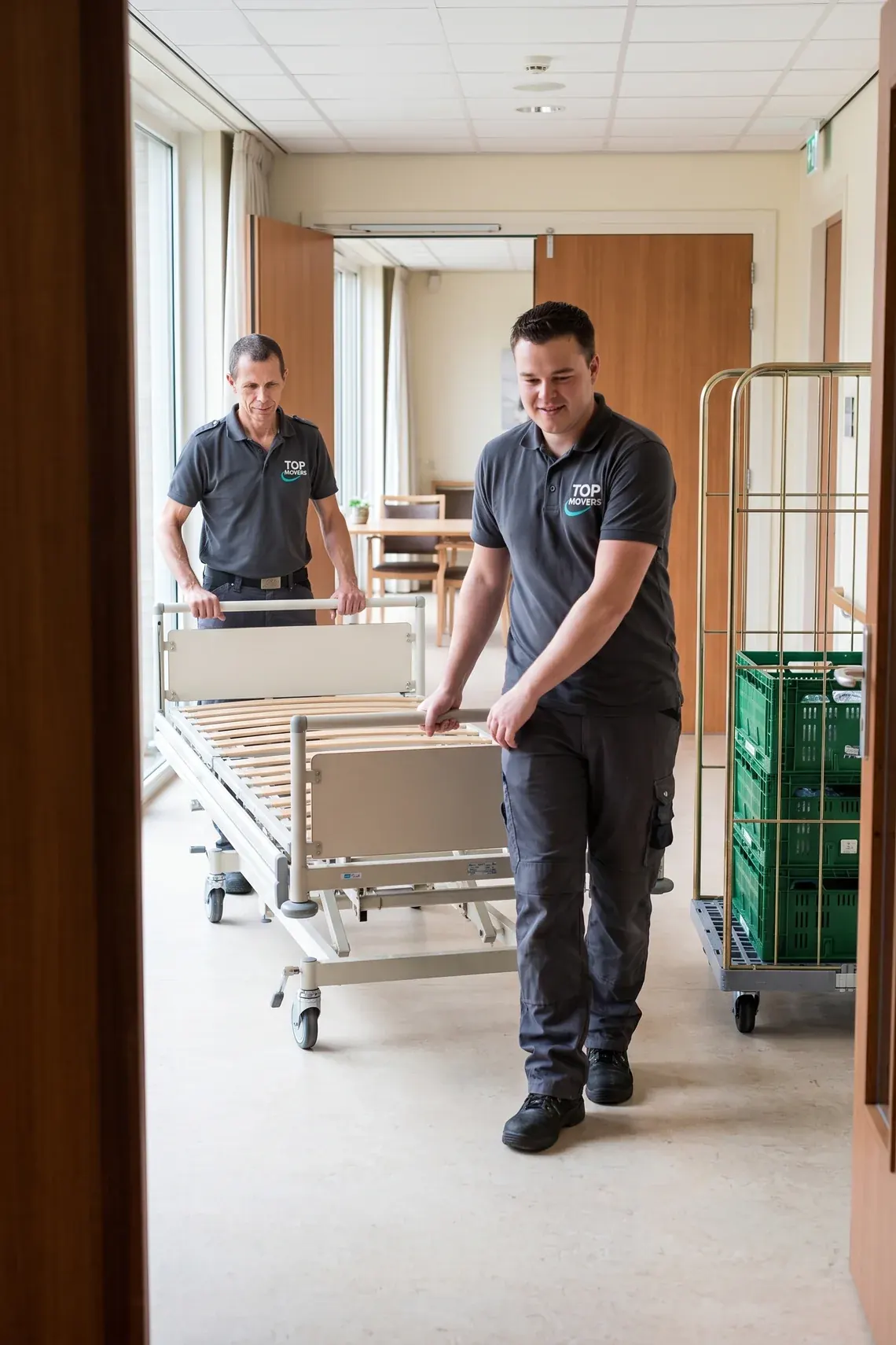 Twee verhuizers rijden een leeg ziekenhuisbed door de gang van een zorgcentrum